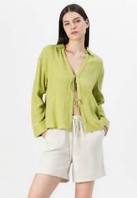 Limoengroene, button-down blouse met een gestructureerde afwerking, met een striksluiting aan de voorkant. Gecombineerd met lichtbeige, shorts met trekkoord.
