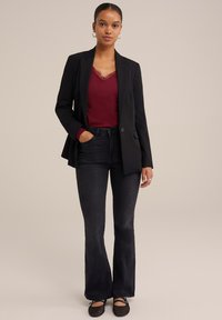 Blazer nero su un top bordeaux con bordo in pizzo, abbinato a jeans svasati scuri e ballerine in rete nere. Texture morbide e vestibilità su misura.
