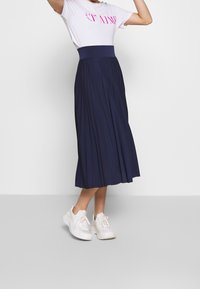 Marinblå plisserad midikjol med hög midja, kombinerad med en vit t-shirt med rosa text och vita sportskor.