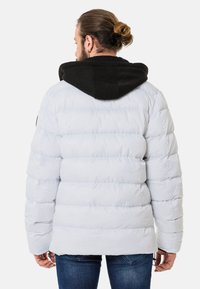 Weiße Puffjacke mit schwarzer Kapuze, mit gesteppten Abschnitten und einer lockeren Passform. Glatte Textur mit leicht glänzendem Finish.