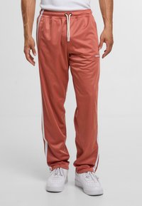 Lässig geschnittene, rosafarbene Sweatpants aus glattem Stoff, mit weißen Seitenstreifen und einem elastischen Bündchen mit Kordelzug.