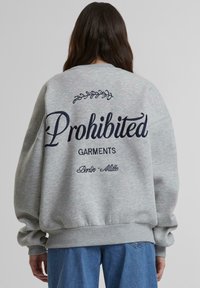 Šedá mikina s tmavomodrým nápisom "Zakázané odevy" na chrbte, s voľným strihom a rebrovanými manžetami a spodným lemom.