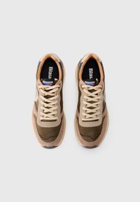 O pereche de sneakers bej și verde măslinie, cu șireti crem și accente albastre, văzuți de sus pe un fundal alb.