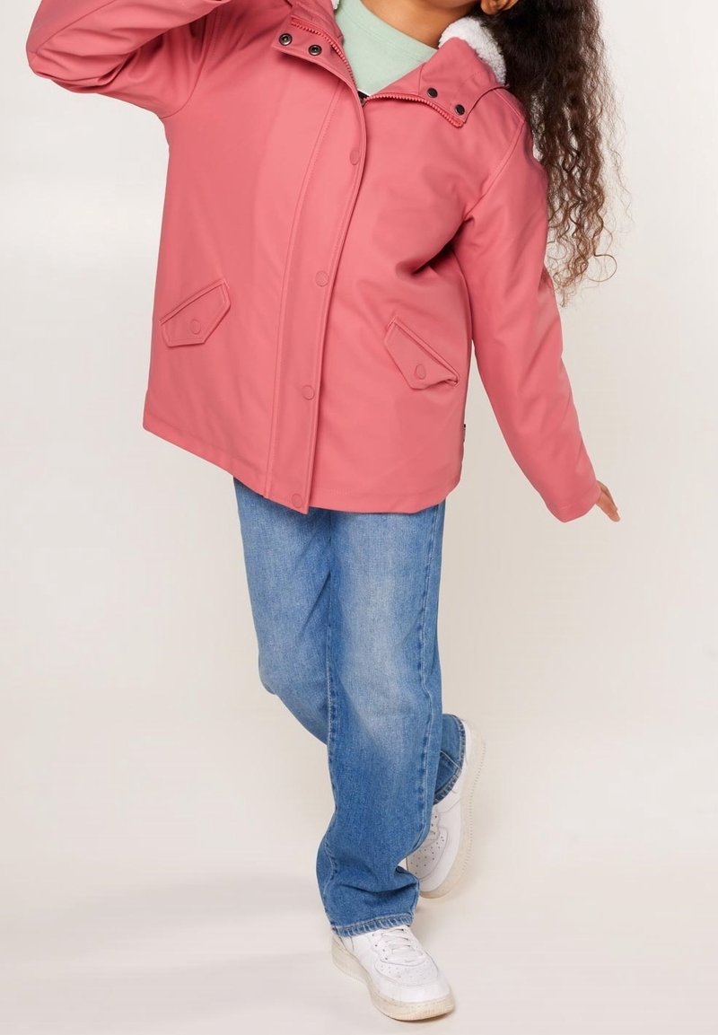 Ljusrosa utomhusjacka med huva, mjukt foder och tryckknappsstängning, i kombination med blå jeans och vita sneakers.