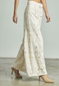 Gonna lunga color crema realizzata in pizzo con motivi intricati, dotata di una cintura larga e una cintura abbinata. Indossata con tacchi beige.