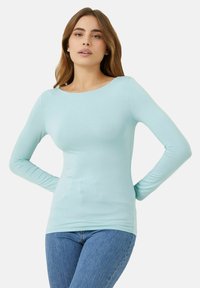 Hellblaues Langarmshirt aus weichem Stretchstoff. Es hat einen runden Halsausschnitt und ein figurbetontes Design, kombiniert mit hellblauen Jeans.