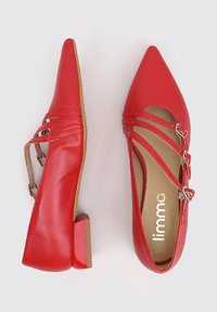 Bailarinas de cuero rojo con puntera puntiaguda, tacón bajo pequeño y detalles decorativos en la correa que incluyen acentos plateados y una plantilla en color marrón claro.