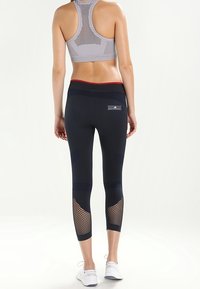 Svarta sportleggings med meshpaneler på nederbenen, en bred midja och en figursydd design. Kombinerat med en grå perforerad sport-bh.