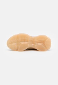 Semelle d'une basket beige avec une semelle extérieure en caoutchouc texturée et segmentée, présentant un motif de bande de roulement en zigzag pour une meilleure adhérence.