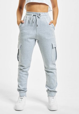Person iført lysegrå cargo joggebukser med snøre i taljen og hvide sneakers, hænder i lommerne, stående mod hvid baggrund.