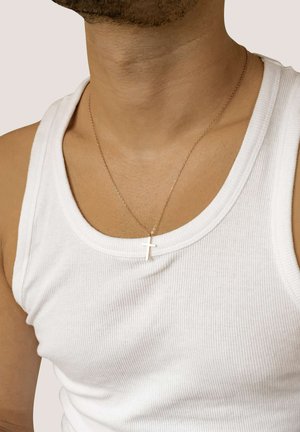 Junge Person mit einer dünnen Kettenkette, an der ein kleines Kreuz hängt, über einem weißen gerippten Tanktop.