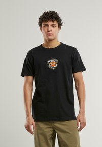 Tricou negru din bumbac cu un grafic frontal al unui tigru și cuvântul "DETROIT" deasupra. Mâneci scurte și design cu guler rotund.