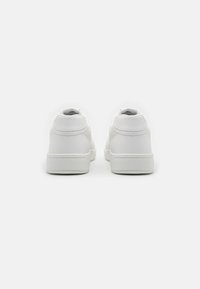 Zapatillas blancas con un upper de cuero suave, puntera redondeada, suela gruesa blanca y detalles de costura minimalistas en el talón.