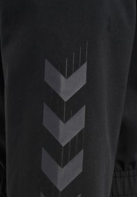 Sort stof med tre nedadvendte reflekterende vinkler arrangeret lodret på en ærme eller bukseben.