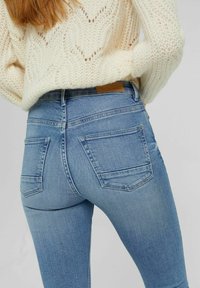 Jeans ajustados de color azul claro con un acabado desgastado, que cuentan con dos bolsillos traseros y una etiqueta de cuero marrón en la cinturilla.