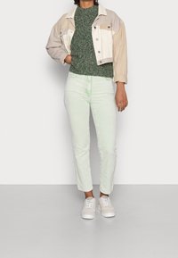 Ljust gröna kordfloddsbyxor, mörkgrön strukturerad tröja och en tvåfärgad kort jacka. Vita sneakers fulländar outfiten.