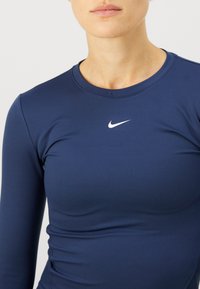 Tamna plava majica dugih rukava za sport, izrađena od glatkog, rastezljivog materijala, sa malim bijelim Nike logotipom na prsima.