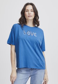 Camiseta de algodón azul con mangas cortas, que presenta "AMOR" bordado en colores contrastantes. Corte holgado con escote redondo.
