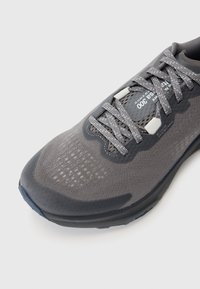 Baskets de sport grises avec tige texturée, détails en maille et accents réfléchissants. Comprend des lacets gris et une semelle rembourrée avec une semelle extérieure bleue.