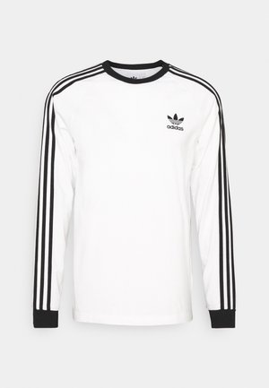 Weißes Adidas Langarmshirt mit schwarzen drei Streifen an den Ärmeln, schwarzem Kragen und Bündchen und schwarzem Adidas-Logo auf der linken Brust.