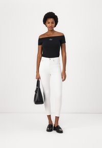 Zwarte off-the-shoulder top met logo, witte hoge taille jeans, zwarte handtas en zwarte instappers. Soepele textuur, strakke pasvorm.