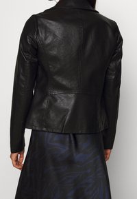 Giacca in pelle nera dal design aderente, con texture liscia e colletto a punta. Presenta dettagli cuciti e un orlo posteriore leggermente svasato.