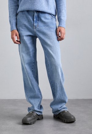 Jeans de denim azul claro con un corte relajado, que cuentan con cierre de cremallera, diseño estándar de cinco bolsillos y detalles de costura visibles.