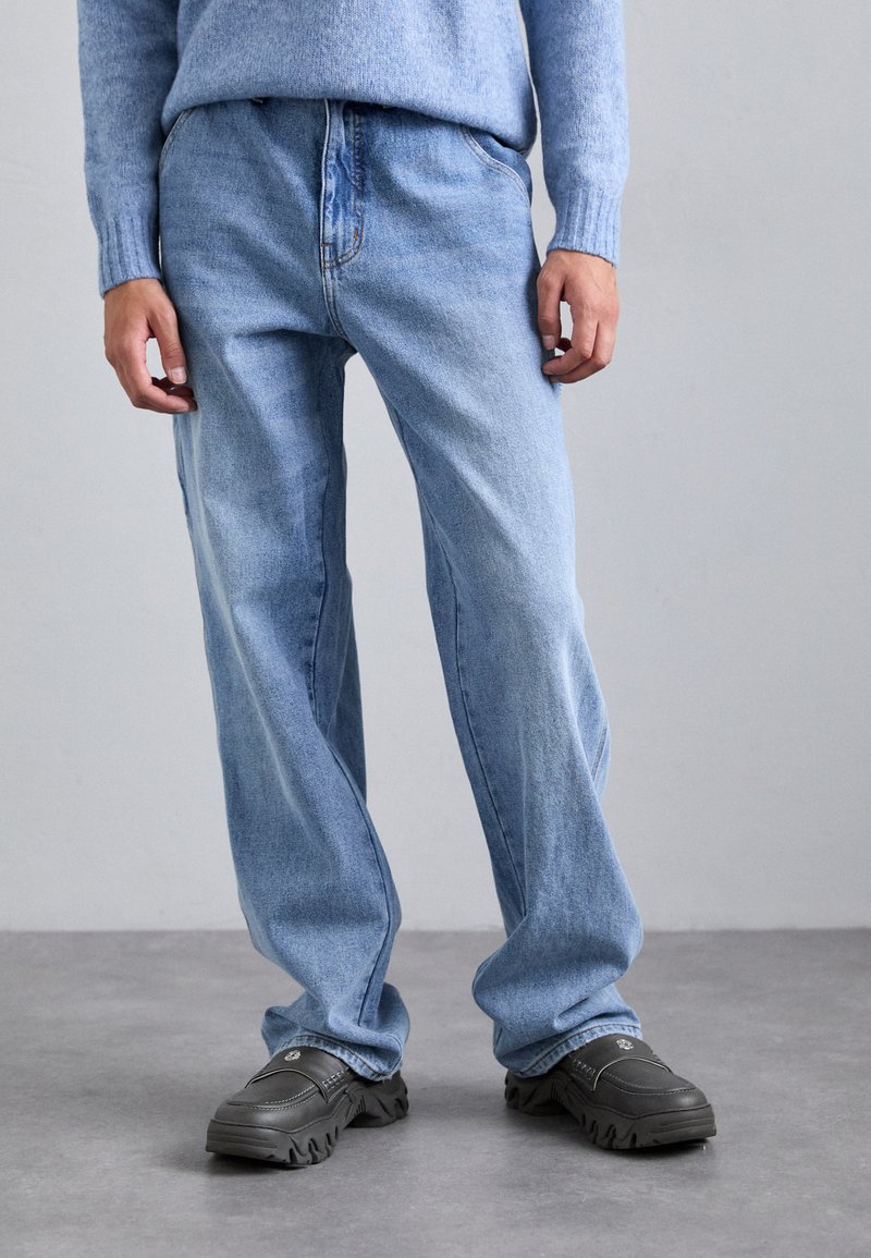 Light blue denim jeans with a relaxed fit, featuring a zip fly, standard five-pocket design, and visible stitching details.