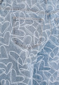 Gai zilgani džinsi ar atkārtotu baltu sirds kontūru rakstu un redzamām aizmugures kabatu šuvēm.