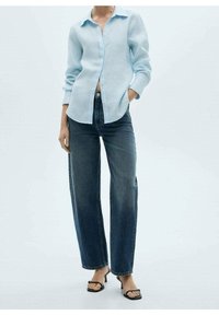 Chemise en lin bleu clair avec un devant à boutons, associée à un jean large à taille haute bleu foncé et des sandales à talons noires.