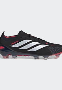 Μαύρο ποδοσφαιρικό παπούτσι με υφασμένη επάνω επιφάνεια, ασημένιες ρίγες, κόκκινες λεπτομέρειες και διαφανές εξωτερικό πέλμα με κόκκινα καρφιά.