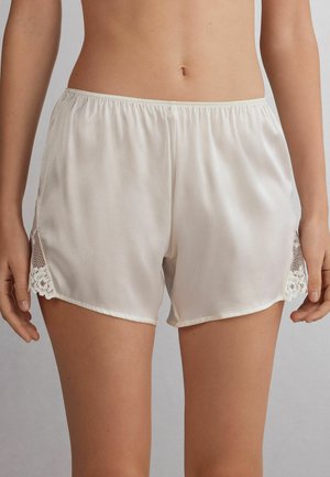Satincreme shorts med avslappnad passform, med spetsdetaljer och mesh på sidorna. Elastisk midja för komfort.
