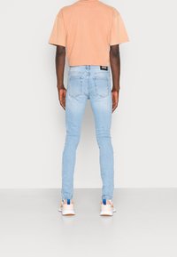 Light blue skinny jeans with a classic five-pocket design, worn with a peach cropped t-shirt and white sneakers featuring blue accents.