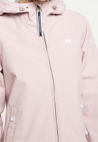 Veste à capuche rose clair avec fermeture éclair, logo de parapluie brodé et accents de boutons-pression sur les poches. Texture de tissu lisse.