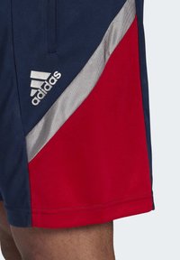 Szorty sportowe Adidas w kolorze granatowym i czerwonym, z ukośnym srebrnym paskiem oraz logo. Wykonane z teksturowanej tkaniny, z wygodnym krojem.