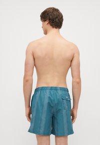 Modré plavkové šortky vyrobené z ľahkého materiálu, s elastickým pásom, bočnými vreckami a jedným zadným vreckom so zapínaním na cvok.