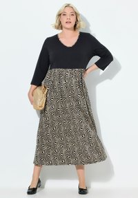 Černý top s výstřihem do V a 3/4 rukávy, kombinovaný s dlouhou vzorovanou sukní v krémových a černých geometrických designech. Doplněno kabelkou.