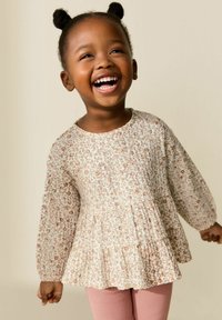 Blusa de estampado floral con mangas largas, base beige claro y bajo con volantes, combinada con leggings rosa de canalé. Textura de tela suave.