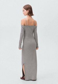 Abito lungo grigio in maglia con design off-the-shoulder, maniche lunghe e spacco laterale. Dettagli in morbida texture a coste visibili, completati da sottili spalline.