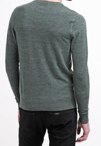 Zielony sweter dzianinowy z długimi rękawami, okrągłym dekoltem i ściągaczem u dołu. Materiał wydaje się miękki i lekko strukturalny, z subtelnym melanżowym wzorem.