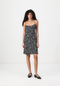 Rochie neagră cu un model abstract de inimă albă, bretele subțiri și ajustabile, corset ajustat, tiv evazat și material ușor. Asortată cu pantofi negri.