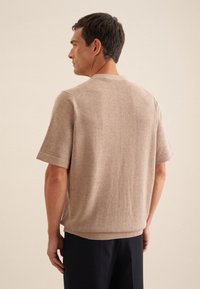 Maglione beige a maniche corte in maglia strutturata, con scollatura rotonda e vestibilità comoda, caratterizzato da cuciture visibili e polsini a coste.