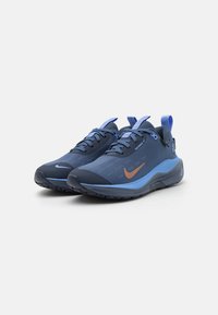 Niebieskie buty sportowe z gładką tekstylną cholewką, kontrastującymi jasnoniebieskimi akcentami, teksturowanymi podeszwami oraz wyraźnym logo Nike w kolorze miedzi.