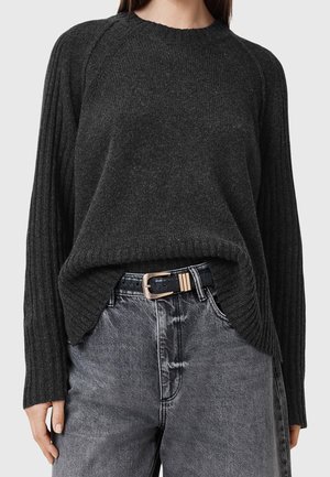 Frau trägt einen dunkelgrauen gerippten Strickpullover, der in hoch taillierte ausgewaschene schwarze Jeans mit schwarzem Gürtel und goldener Schnalle gesteckt ist.