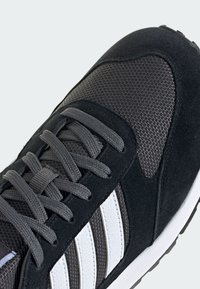 Baskets noires et grises en matériaux mesh et daim, avec des rayures blanches, des lacets gris et une surface texturée.
