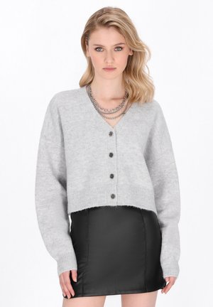 Beskåret grå cardigan med V-hals, fem sorte knapper, ribbet kant og lange ærmer, parret med en sort læder mini-nederdel.