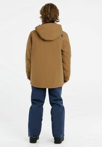 Braune wasserdichte Jacke mit Kapuze, ausgestattet mit elastischen Bündchen, kombiniert mit dunkelblauen wasserdichten Hosen, von hinten betrachtet.