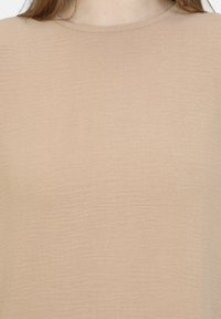 Top beige chiaro a maniche corte con scollatura tonda. La texture appare leggermente stropicciata, dando un aspetto morbido e informale.