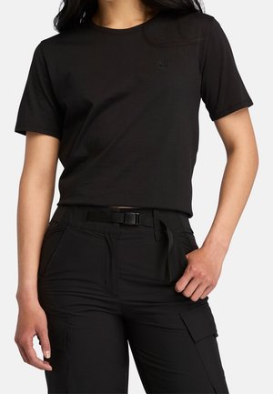 Musta puuvillainen T-paita, jossa on lyhyet hihat ja pyöreä pääntie, rintakehässä hillitty kirjailtu logo. Yhdistetty mustiin cargo-housuihin.