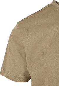 Kortermet t-skjorte i beige stoff, med en glatt tekstur og standard rund hals med subtile sømdetaljer.